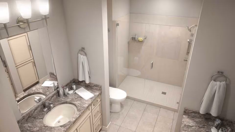 A clean bathroom with a marble countertop vanity and sink, toilet, and a glass-enclosed walk-in shower.