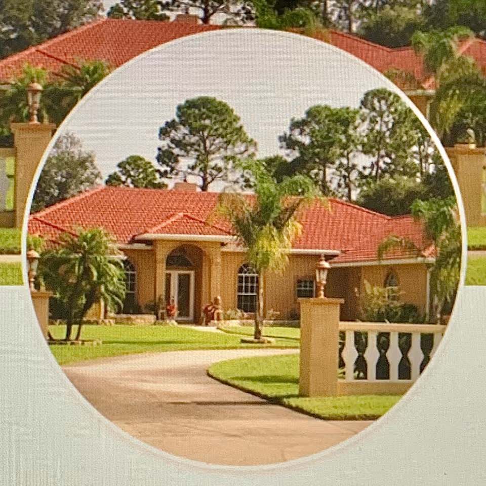 Front view of a Mediterranean-style single-story house with a red tile roof, palm trees, and a curved driveway.