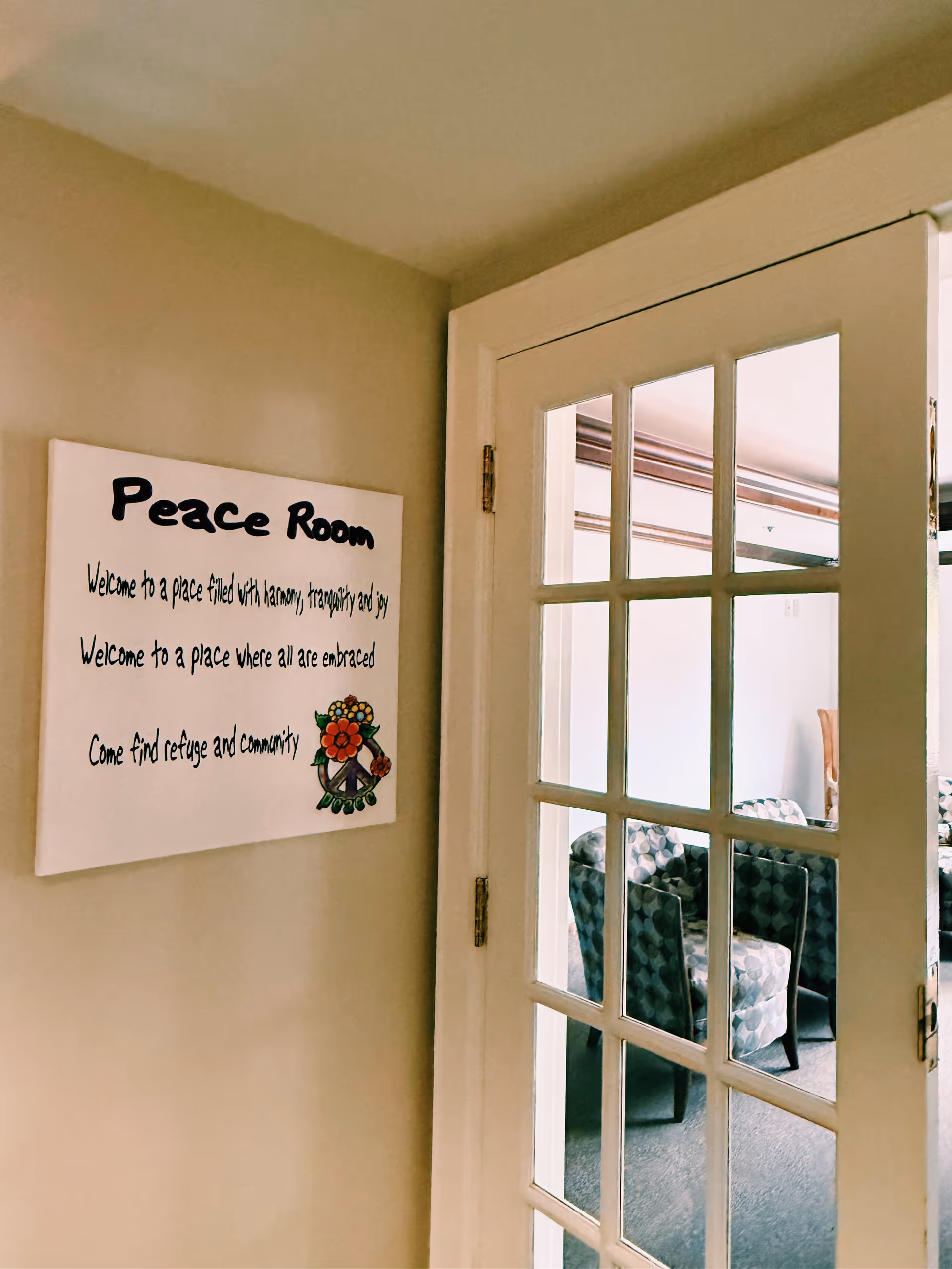 Open glass-paned door leading into a 'Peace Room' with a sign on the wall and patterned armchairs visible inside.