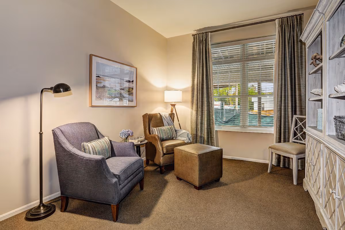 Cozy sitting area with two armchairs, an ottoman, a floor lamp, and a window with curtains.