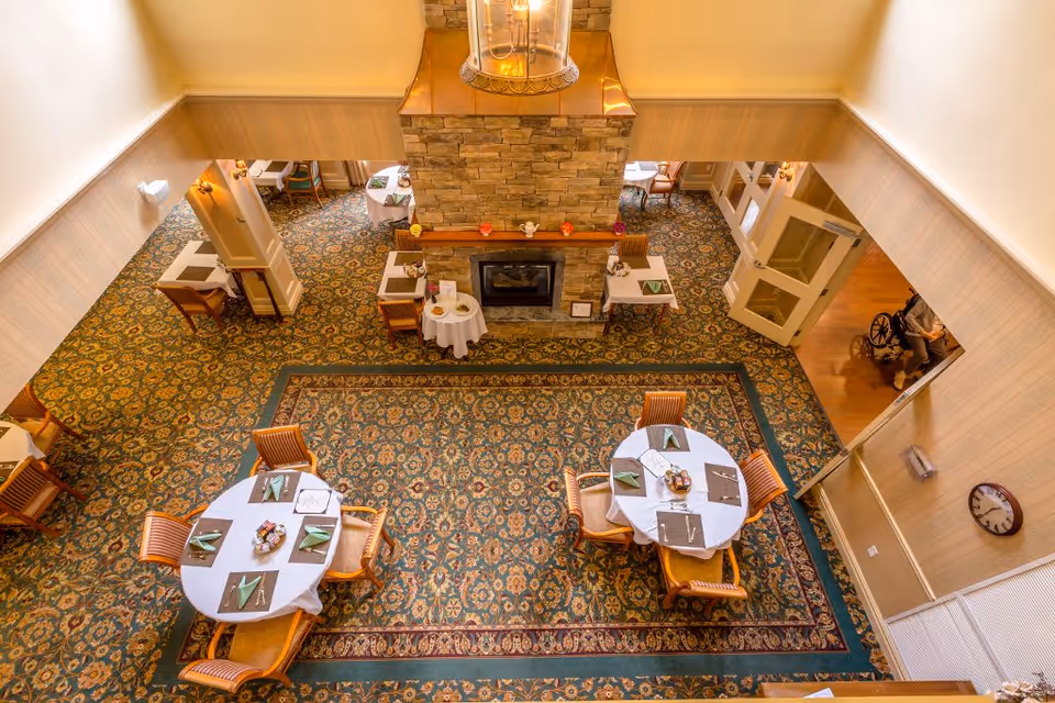 Overhead view of a dining area with round tables set for meals around a central stone fireplace.