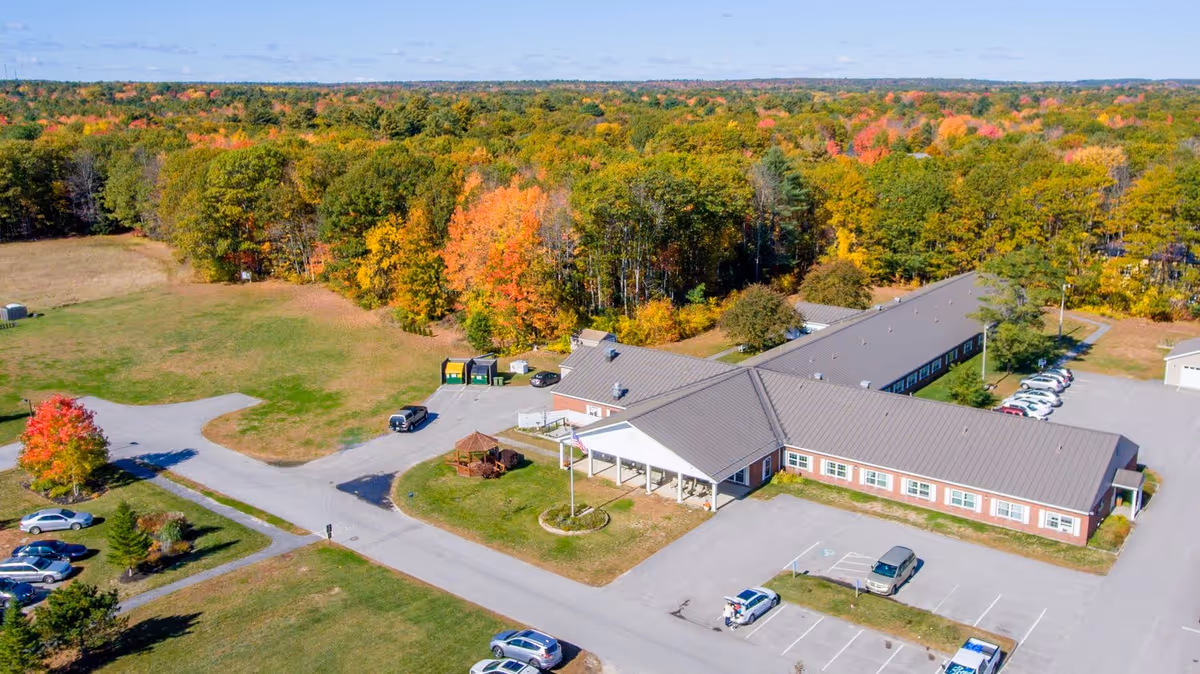 Aerial view of a single-story senior living facility with a parking lot and surrounding trees showing fall colors.