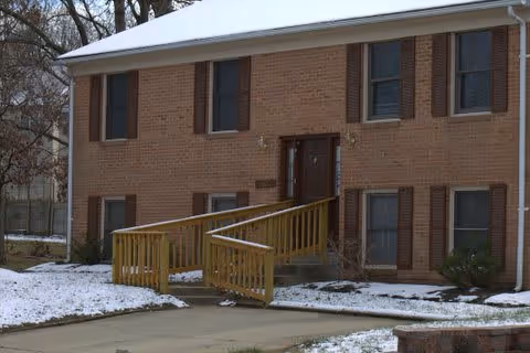 Two-story brick residential building with a wooden wheelchair ramp to the main entrance and light snow on the ground.
