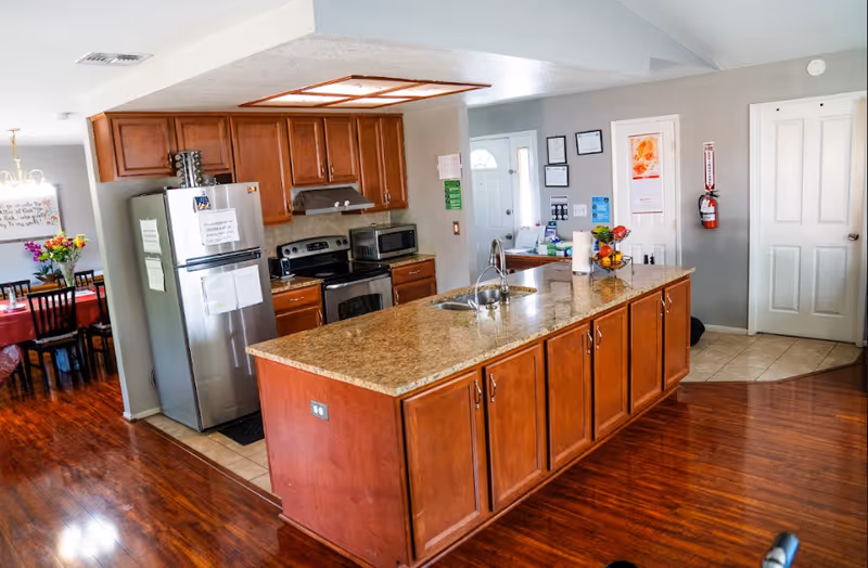 Open-concept kitchen with granite island, stainless appliances, wooden cabinets, and adjacent dining area.