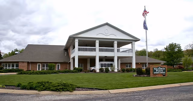 Front exterior of Solarbron Family-First Senior Living facility featuring a white-columned portico, flagpole, and landscaped lawn.
