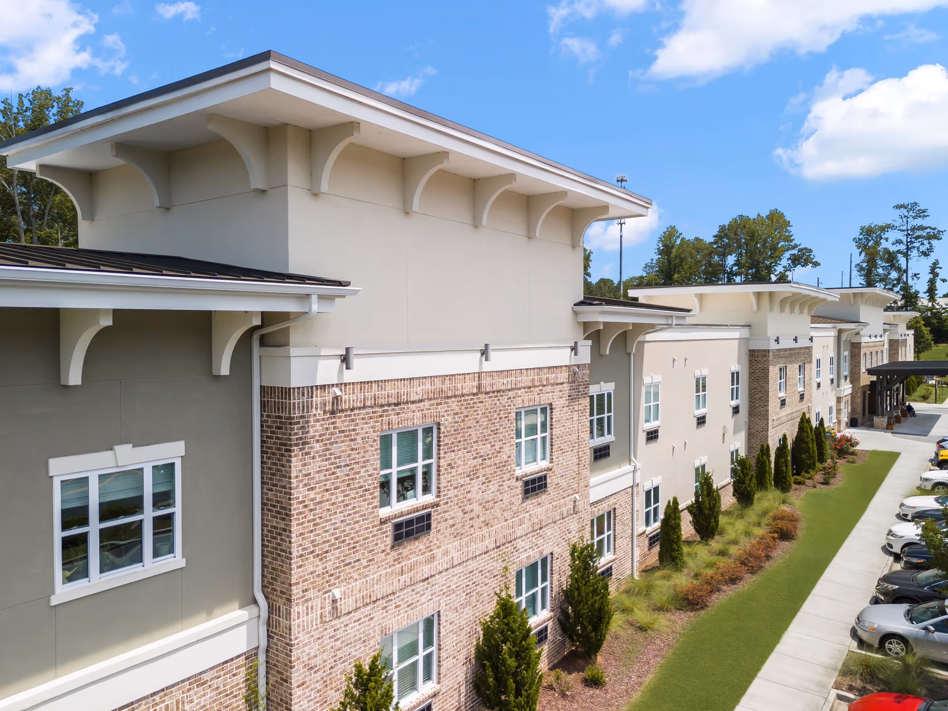 Exterior front facade of a multi-story brick and stucco senior living building with landscaped lawn and parking.