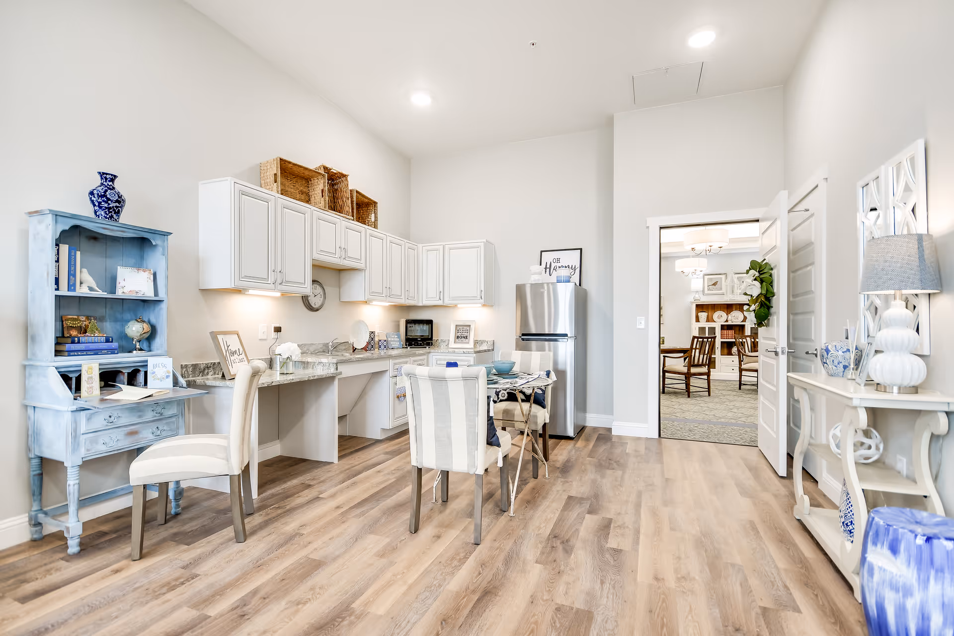 Bright, open kitchenette and dining area with white cabinets, a small table and chairs, and decorative furnishings.