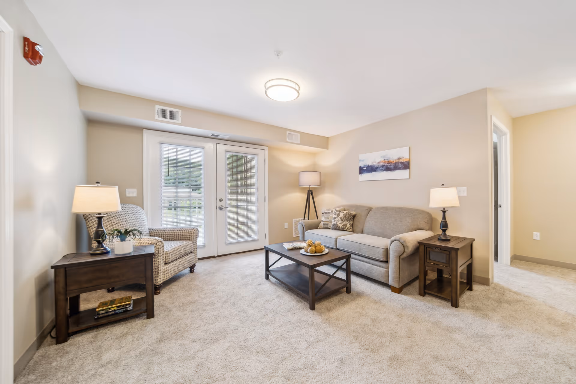 Bright furnished living room with a sofa, armchair, coffee table, side tables and French doors to the outside.
