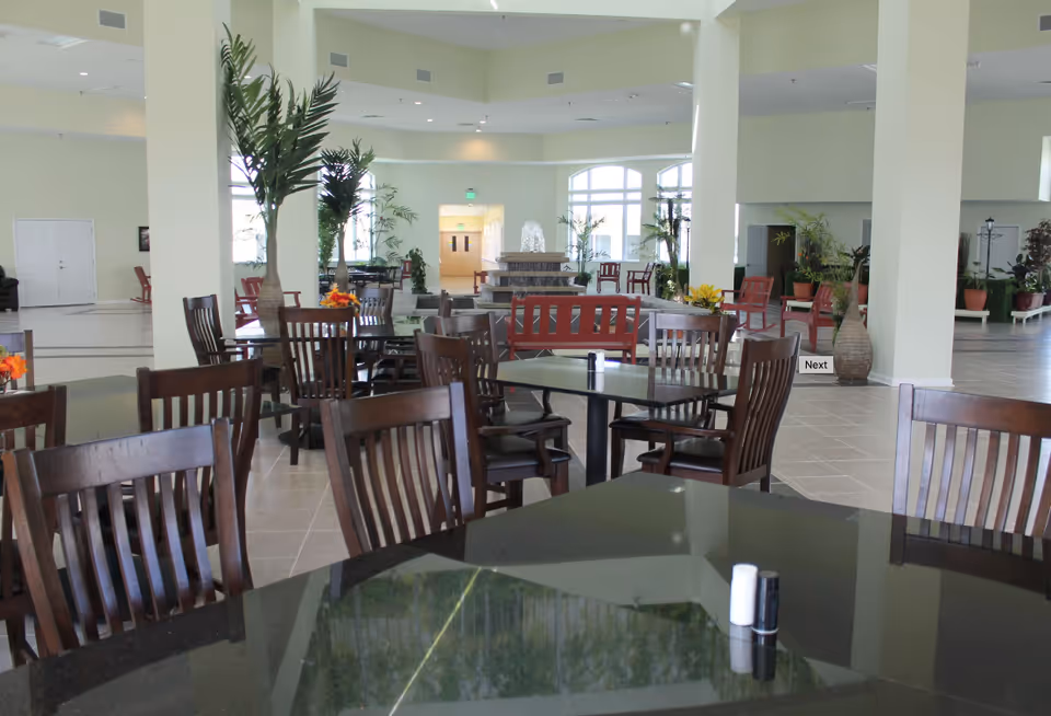 Spacious indoor dining area with dark wood tables, chairs, plants, and a central fountain.