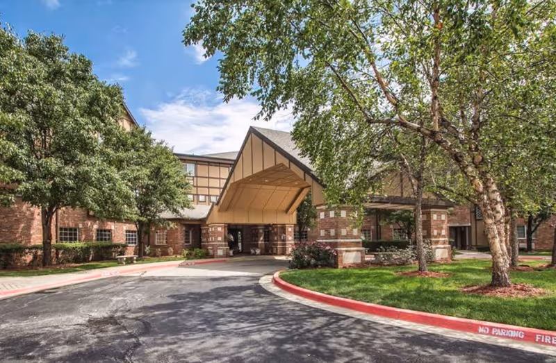 Covered front entrance of a brick senior living building with a porte-cochere, circular driveway and trees.