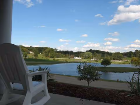 White plastic chair on a covered patio overlooking a lake and green landscape.