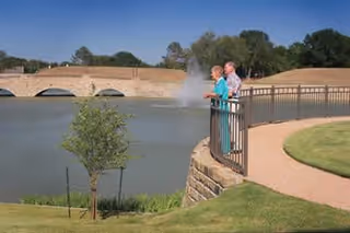 Two residents stand by a railing overlooking a fountain at an outdoor pond.