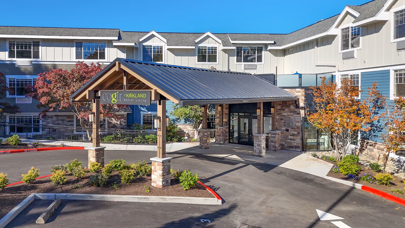 Front entrance of COGIR Senior Living with a covered porte-cochere, landscaping, and a visible sign.