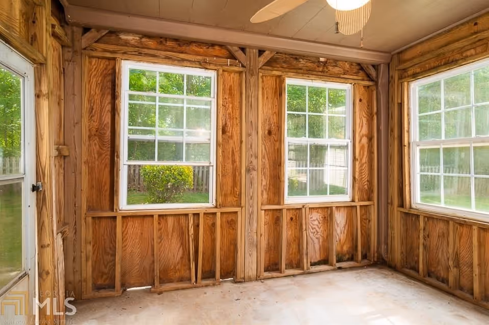 Unfinished wooden sunroom or enclosed porch with three large windows and exposed studs.