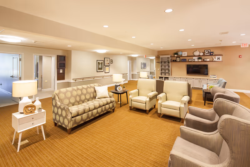 Spacious senior living lounge with sofas, armchairs, side tables and a wall-mounted TV.