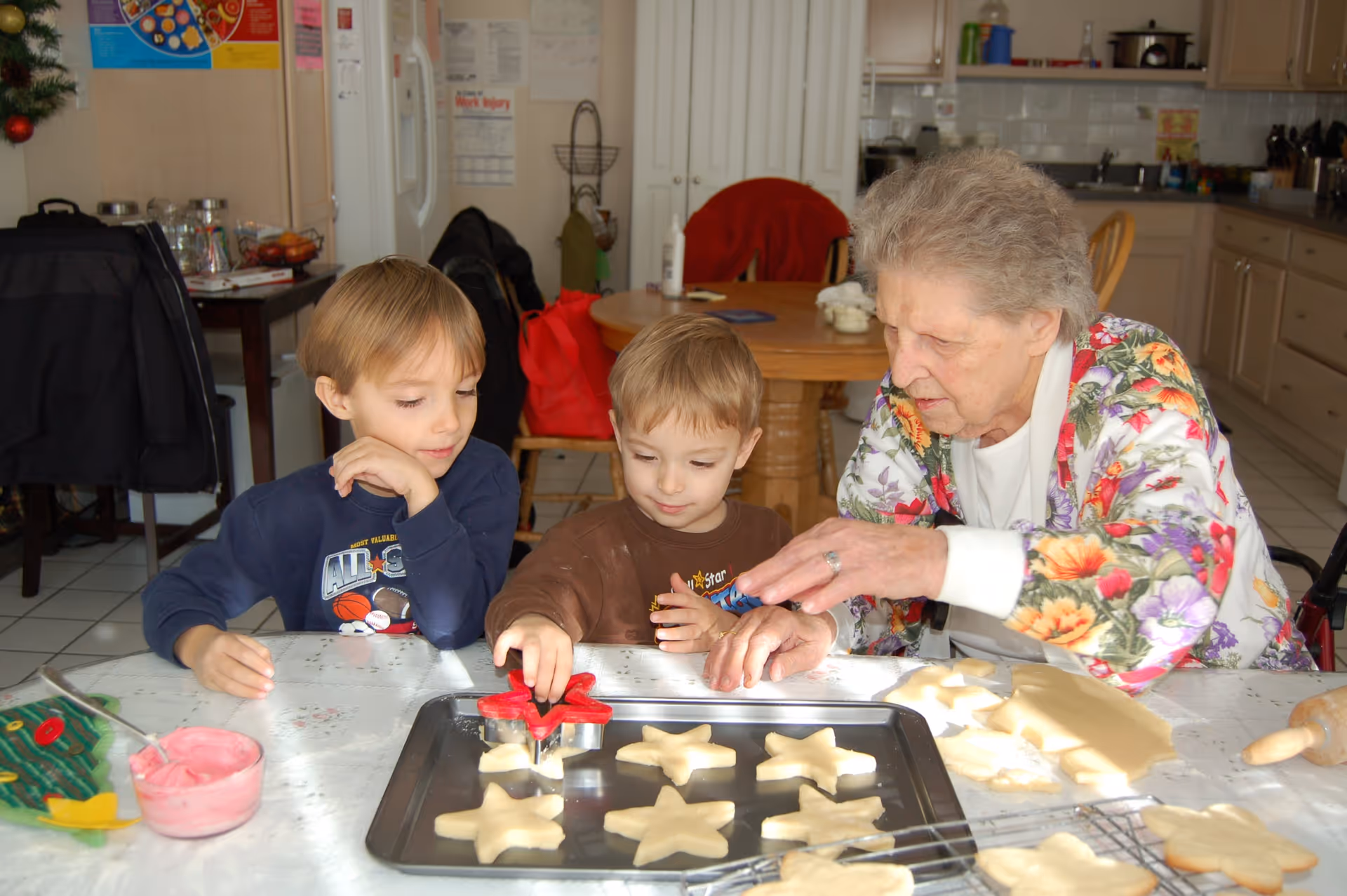 An elderly woman and two young boys cutting star-shaped cookies on a baking tray in a kitchen.