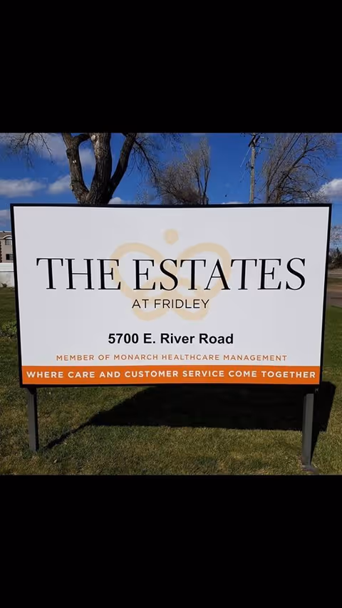 Outdoor roadside sign on grass reading "The Estates at Fridley" with the address and management tagline.