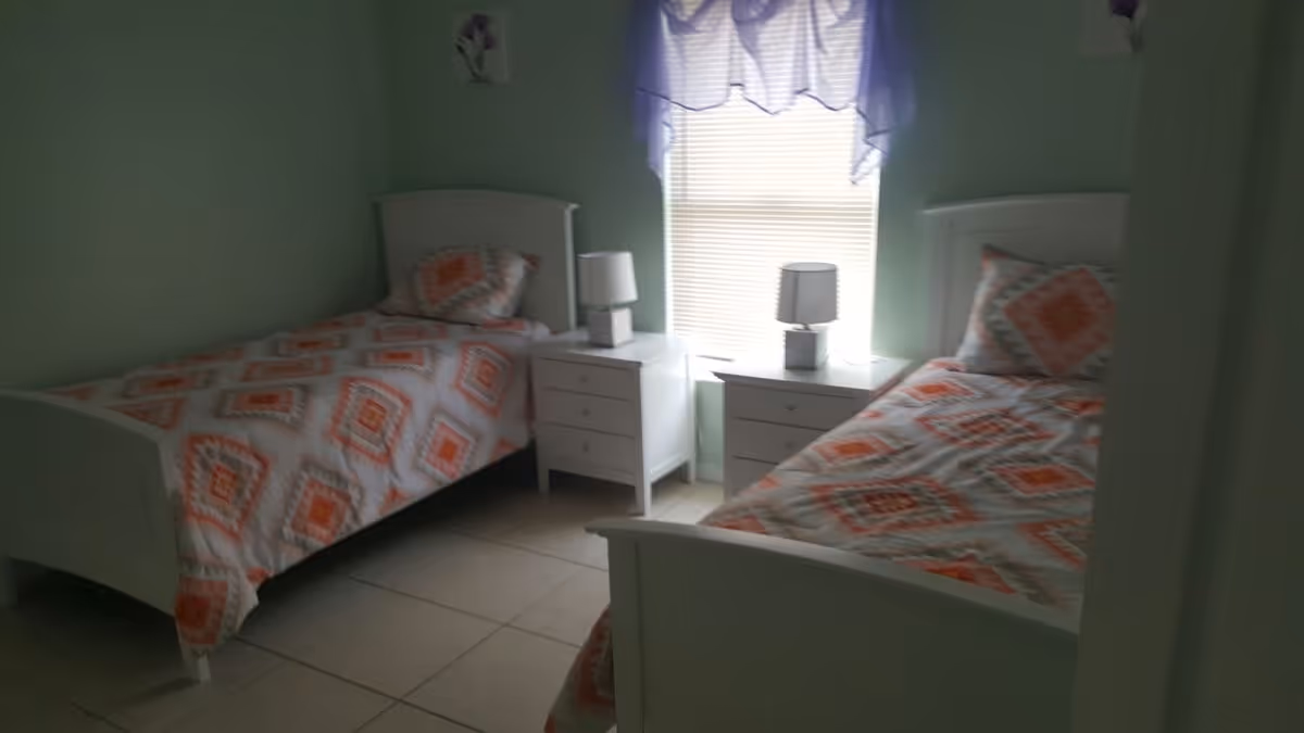 A softly lit bedroom with two twin beds, matching nightstands and lamps beside a central window.