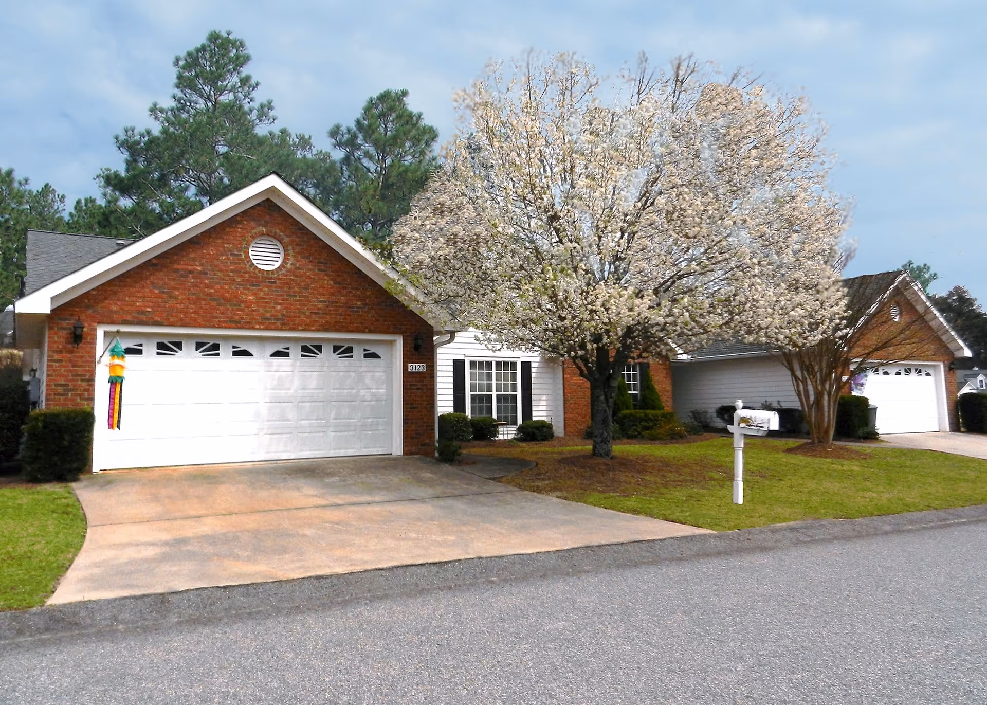 Brick house with two white garage doors and a blossoming tree in the front yard.