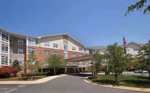 Exterior view of Arbor Terrace Herndon, multi-story senior living building with trees and covered entrance.