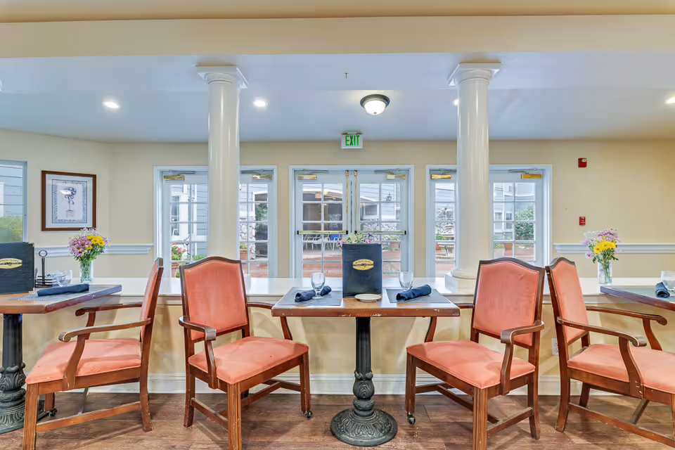 Dining area with wooden tables and red upholstered chairs facing glass doors and white columns.