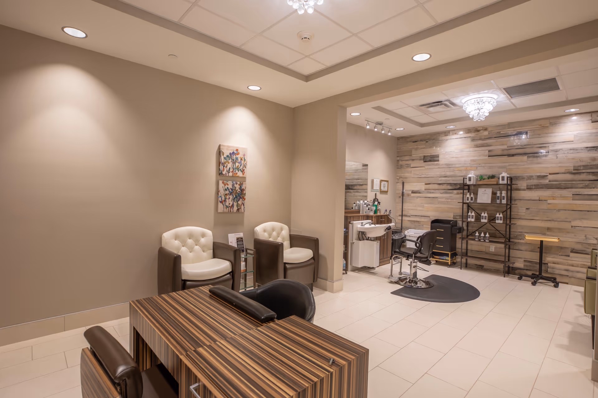 Interior salon area with a manicure table, salon chair, tufted waiting chairs and wood-accent wall.