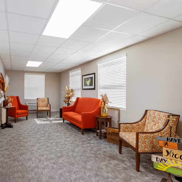 Well-lit seating area with orange sofas and patterned chairs along a windowed wall.