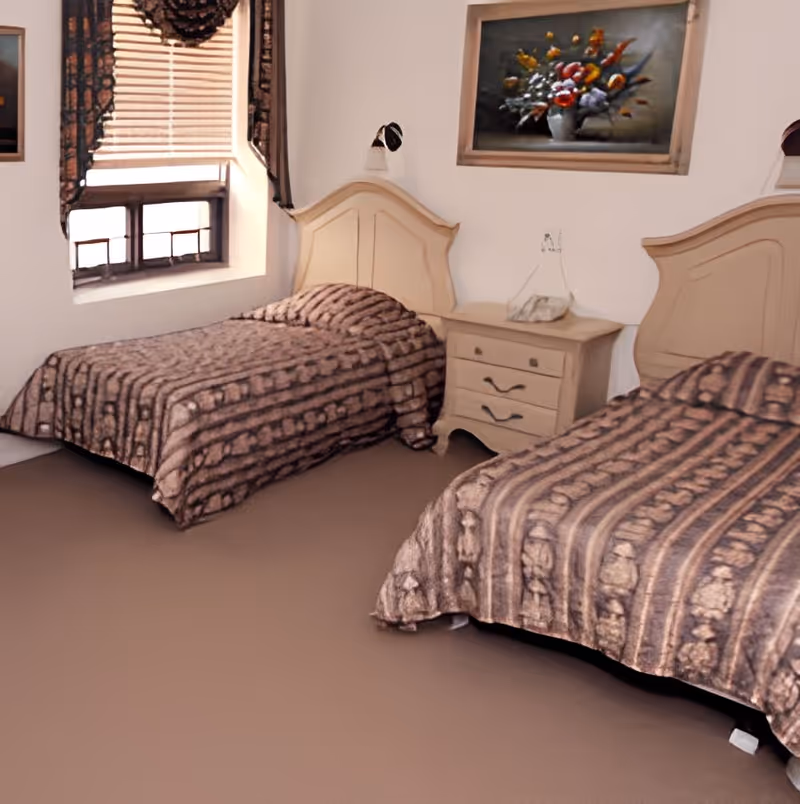 Two twin beds with patterned bedspreads and a nightstand between them in a bedroom with a window and wall art.