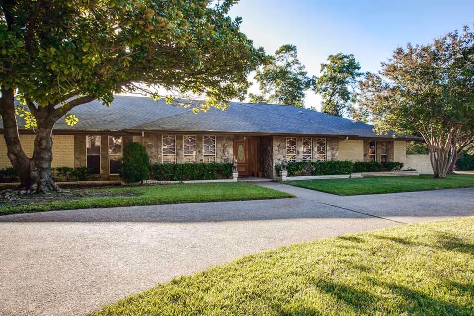 Single-story building with a stone and brick exterior, surrounded by green grass and trees, under a clear blue sky.