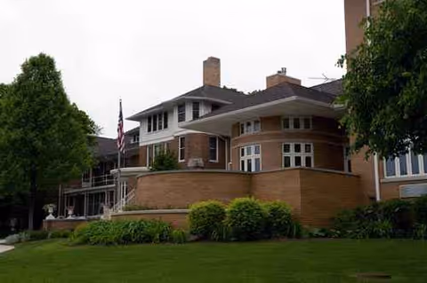 Brick senior living facility with a curved front, flagpole, and manicured lawn.