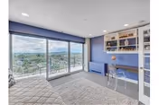 Bright bedroom with floor-to-ceiling windows opening to a balcony, a bed on the left, and built-in shelving and desk against a blue accent wall.