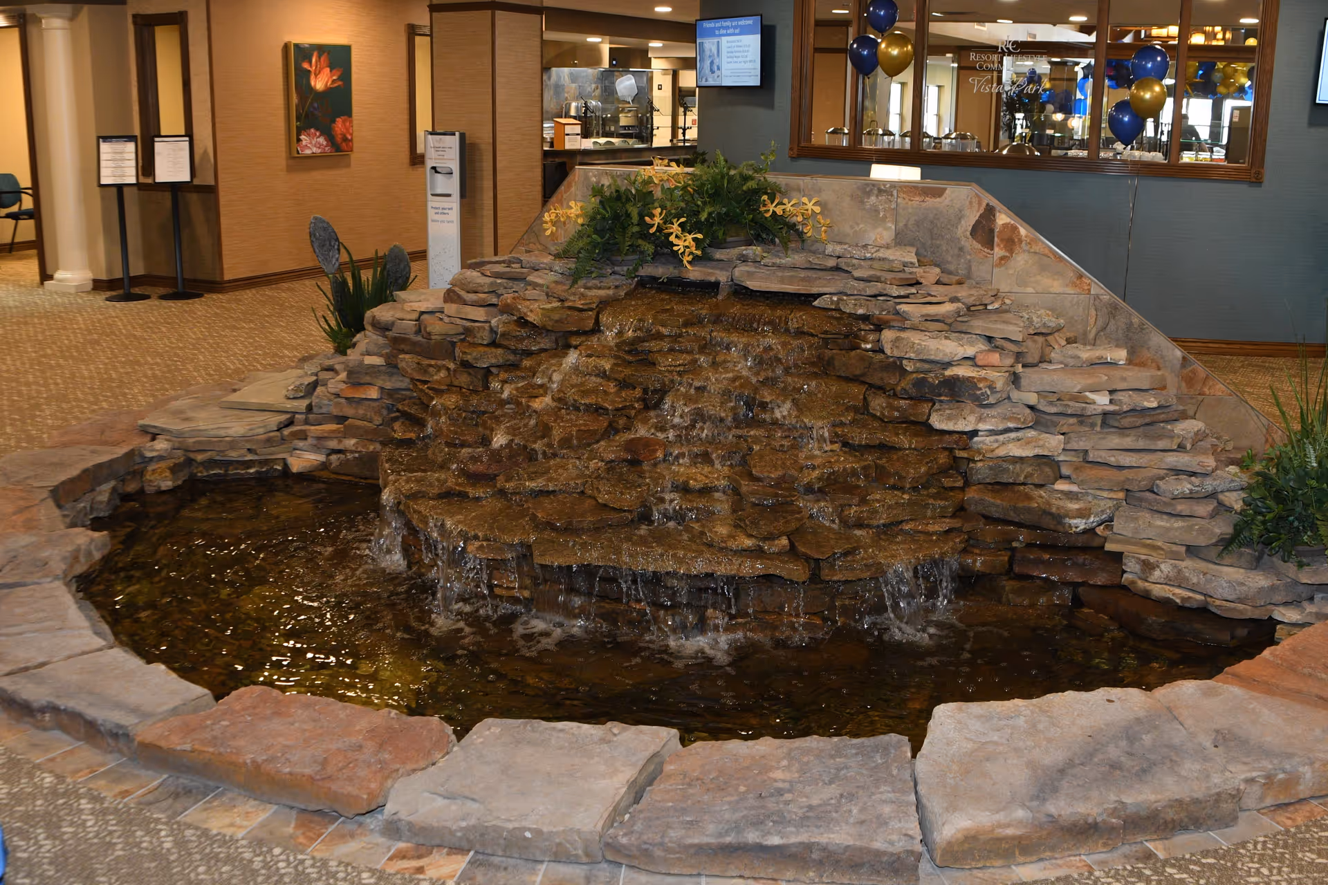 Indoor stone water fountain with a cascading waterfall in a retirement community lobby.