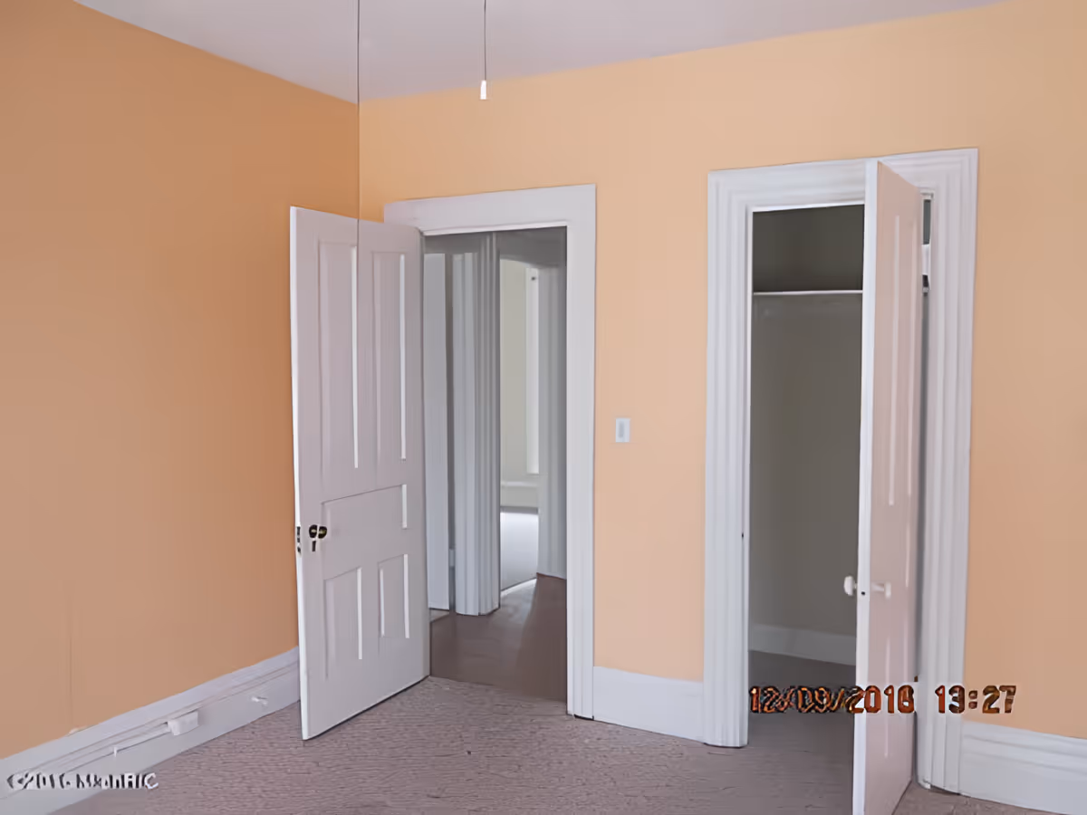 Empty room with peach-colored walls, white trim, and two open doors. One door leads to a hallway and the other to a small closet. The floor is carpeted in a light color.