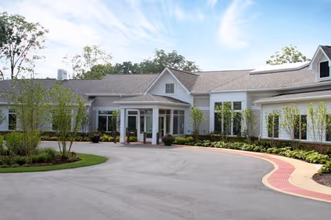 Exterior view of a single-story senior living center with a curved driveway and glass entrance.