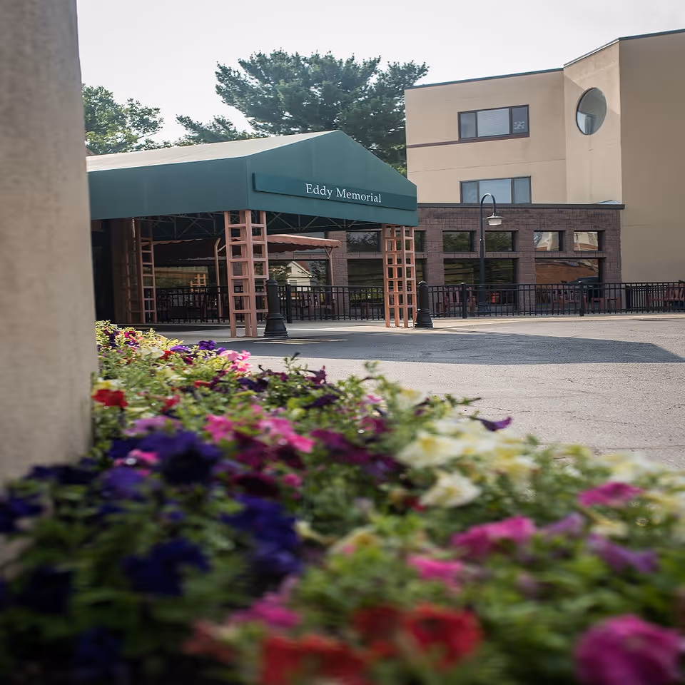 Entrance canopy reading "Eddy Memorial" at the front of a senior living facility with colorful flowers in the foreground.