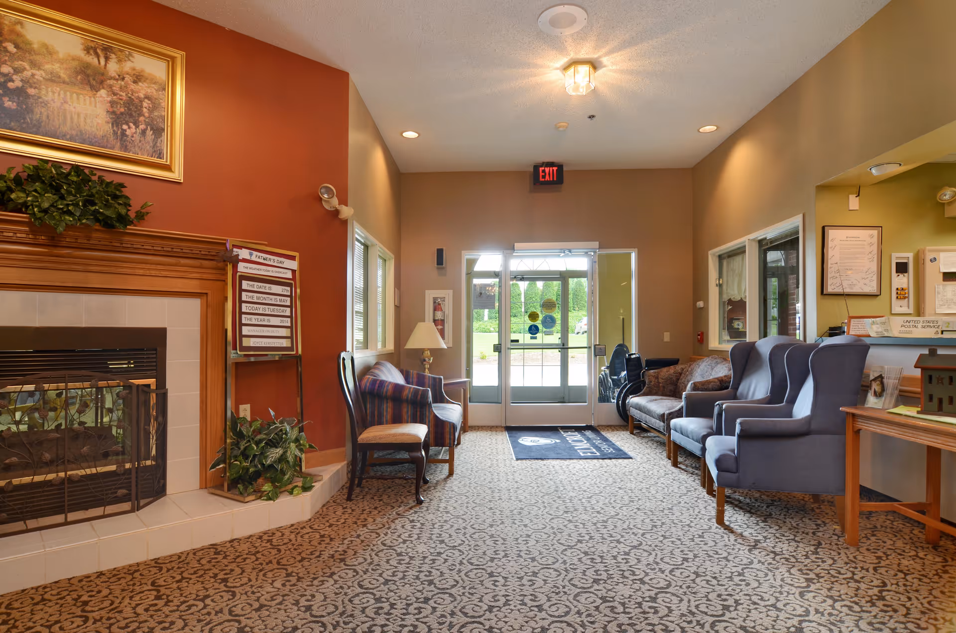 Reception lobby of a senior living facility with seating, a fireplace, and glass entrance doors.