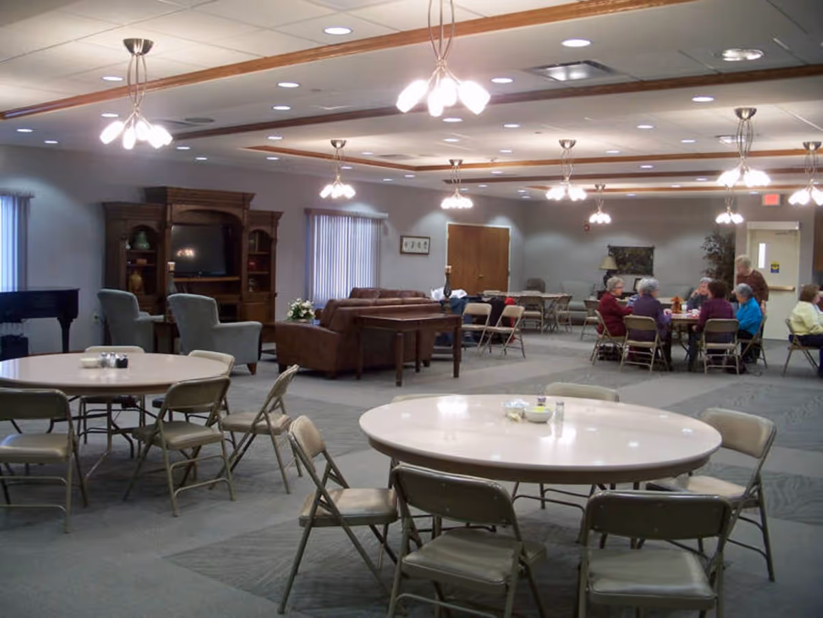 Large multipurpose dining and lounge room with round tables and folding chairs and a group of seniors seated at one table.