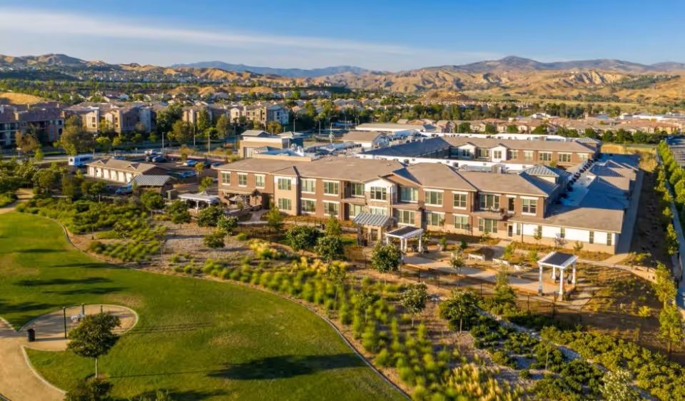 Aerial view of the Oakmont of Valencia senior living building with landscaped grounds, outdoor seating areas, and surrounding parkland and hills.