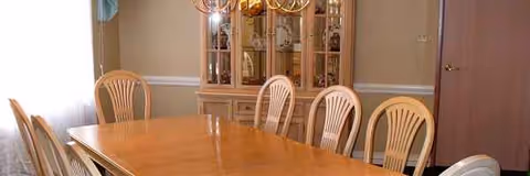 Long wooden dining table with cream-colored plastic chairs in a formal dining room.