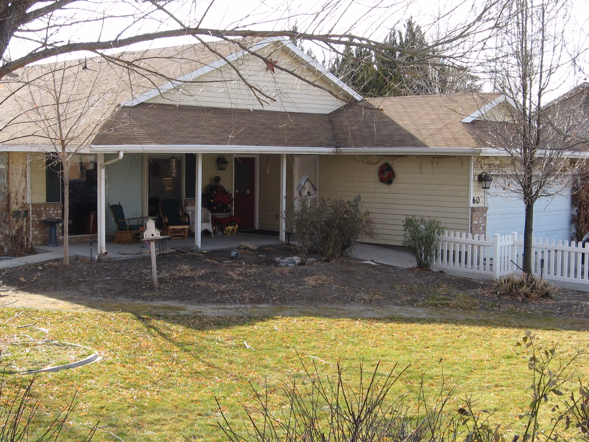 A single-story villa with a covered front porch, outdoor seating, wreath, and yard.