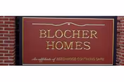 A maroon sign with gold lettering mounted on a brick wall that reads 'BLOCHER HOMES' with smaller text below stating 'An affiliate of BEECHWOOD CONTINUING CARE'.