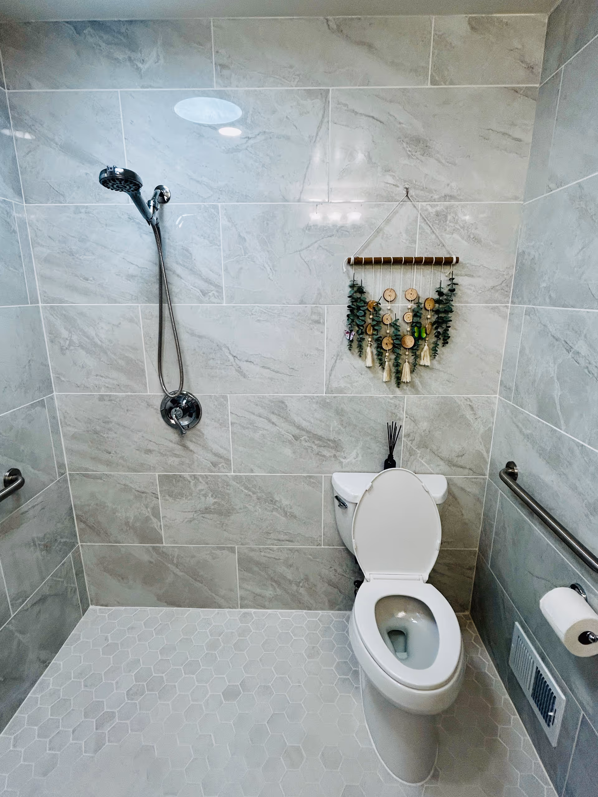 A modern bathroom with a shower, toilet, and decorative wall hanging.