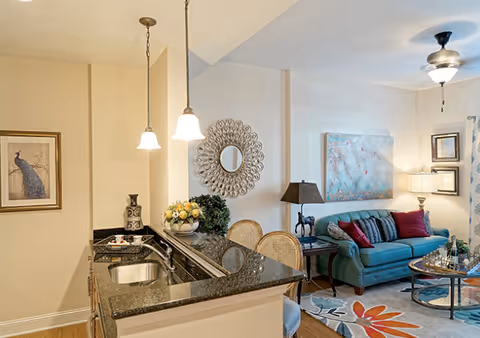 Open-plan living area with a granite-topped kitchen island leading to a seating area with a teal sofa and decorative wall art.