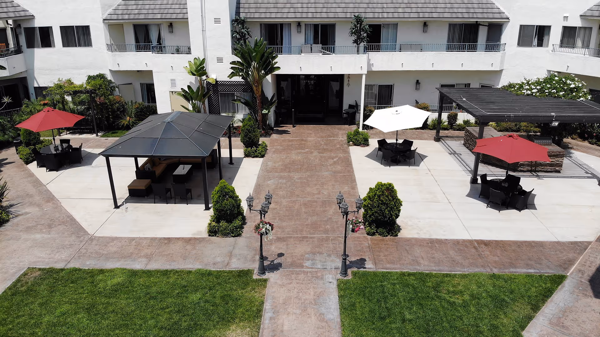 Courtyard and entrance of a white retirement building with patios, umbrellas, gazebos, and a central walkway.