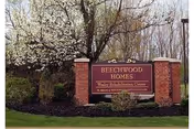 Brick entrance sign that reads "Beechwood Homes" surrounded by landscaping and a flowering tree.