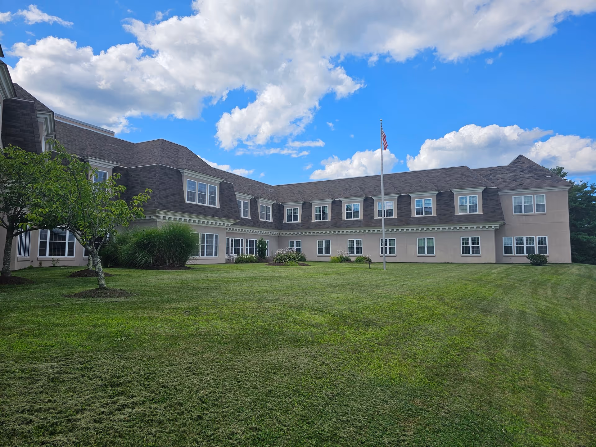 Two-story building front viewed across a well-manicured lawn with a flagpole under a blue, partly cloudy sky.