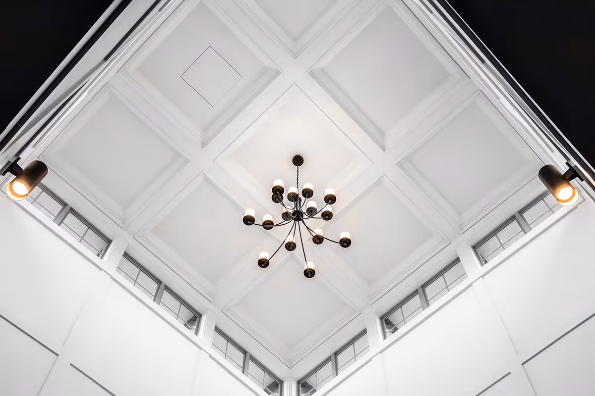 View looking up at a white coffered ceiling with a modern multi-arm chandelier and corner spotlights.