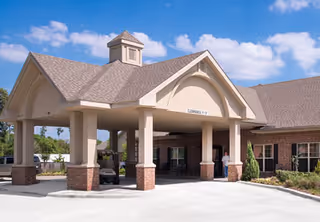 Front entrance of a senior living facility with a covered porte-cochere, brick facade, and blue sky.