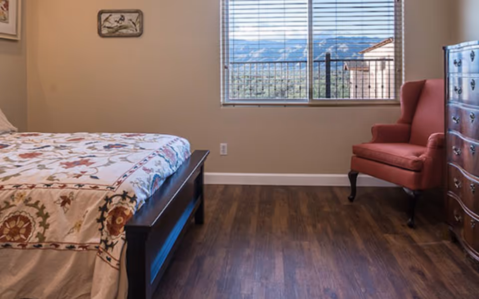 Furnished bedroom featuring a bed, red armchair, dresser, and window view.