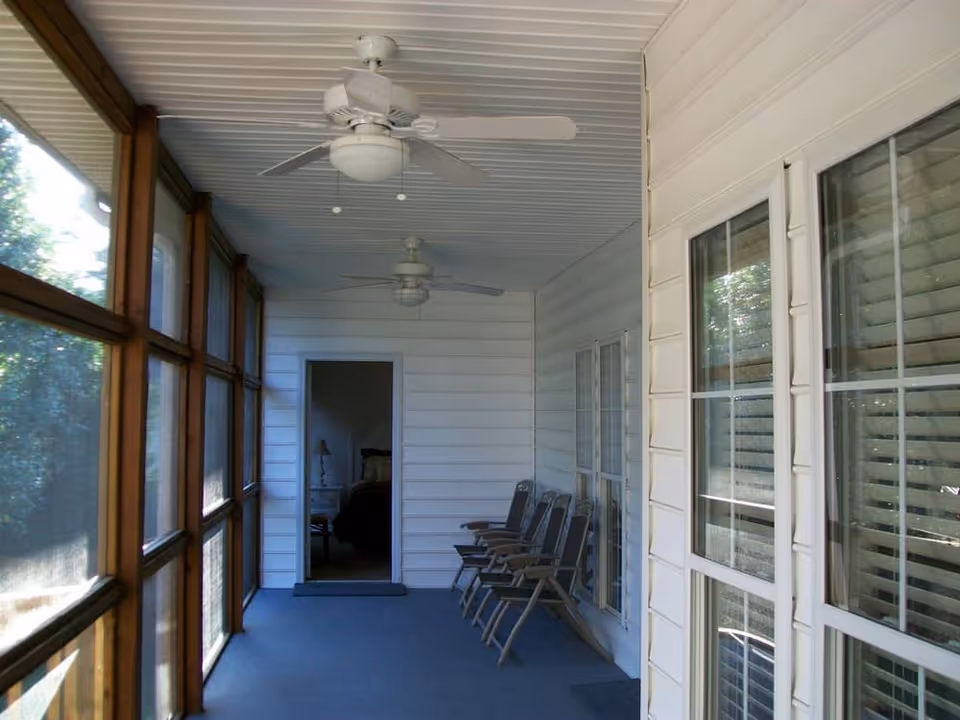Enclosed screened porch with ceiling fans and row seating facing a doorway to an interior room.